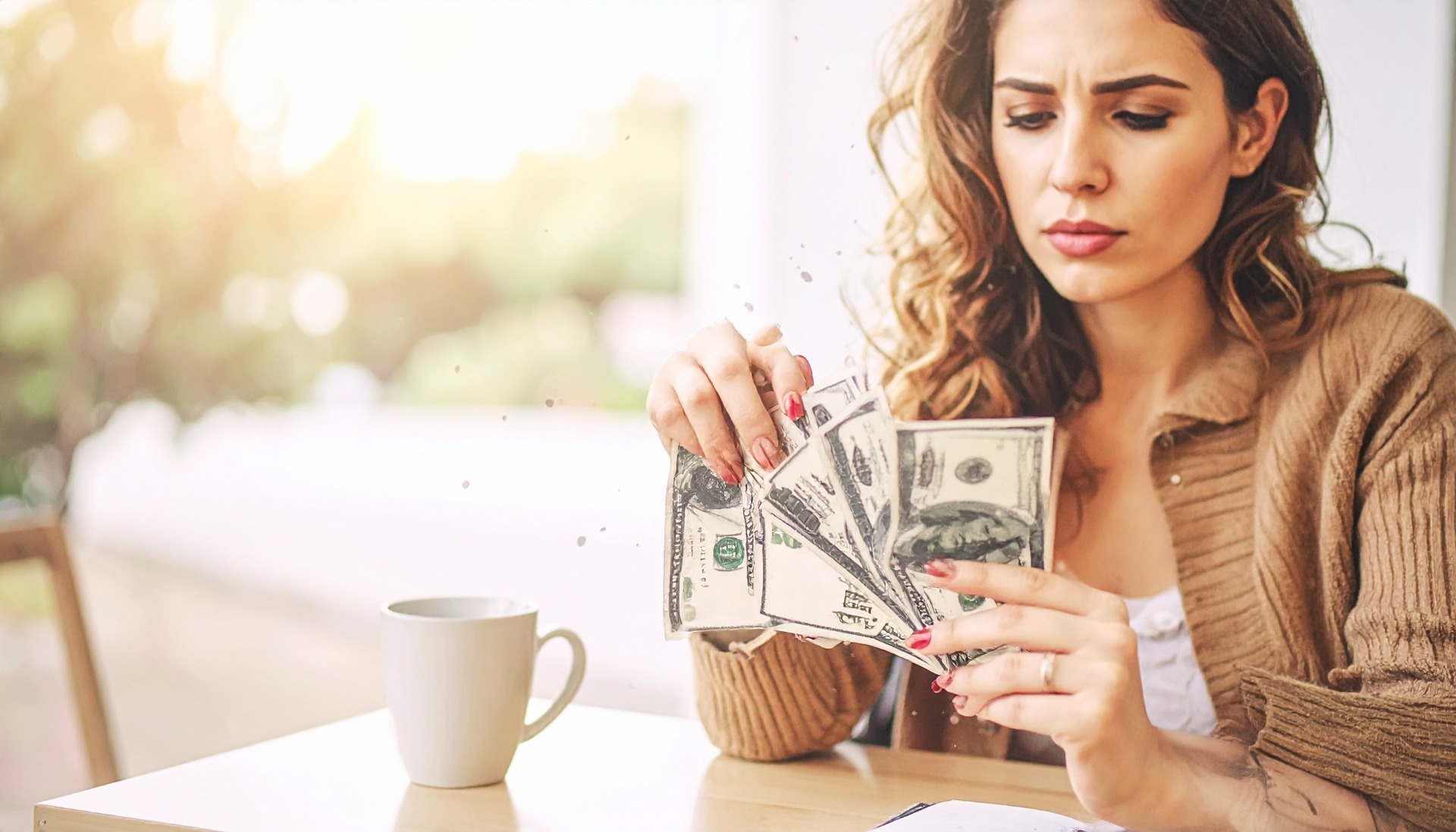 Woman counting US dollar bills at a table, warm light, blurred background, focused expression.